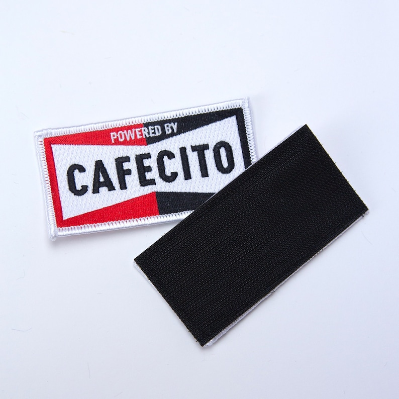 May include: White patch with red and black accents. The patch has the text "POWERED BY" and "CAFECITO" in black lettering.