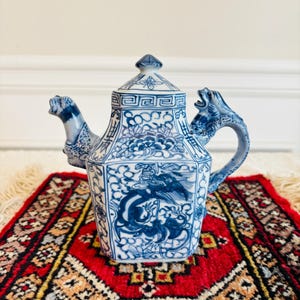 May include: A blue and white porcelain teapot with a dragon handle and lid. The teapot is decorated with a floral pattern and a dragon design.