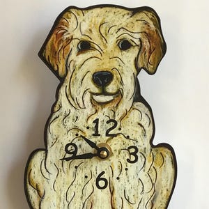 Op de afbeelding: Een witte en bruine hondenklok met een slingerstaart. De wijzerplaat van de klok heeft zwarte Romeinse cijfers en zwarte wijzers.