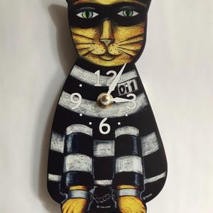 May include: A whimsical cat-shaped wall clock with a black and white striped body and a yellow face wearing a black mask. The clock features white numbers and hands, and yellow paws. The clock is a unique decorative item.