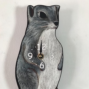 May include: A gray and white squirrel-shaped clock with black clock hands and white numbers. The clock face has the numbers 12, 9, 3, and 6.