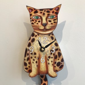 Op de afbeelding: Een bruine en zwart gevlekte kattenklok met een zwarte wijzer en witte cijfers. De wijzerplaat geeft 12, 9, 6 en 3 aan.