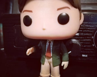 May include: A green and brown pop culture figure wearing a plaid shirt and a red tie. The figure has a large head with black eyes and a white face.