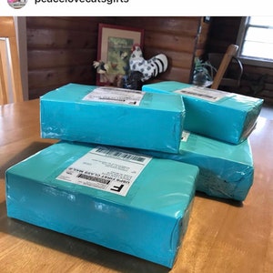 Puede incluir: Una pila de cuatro cajas de color azul turquesa con una etiqueta blanca en la caja superior que dice "USPS First Class Mail".