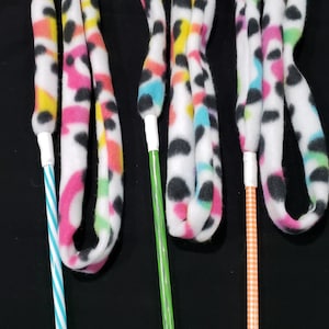 May include: Three colorful cat toys with different colored striped sticks. The toys are made of white fabric with black spots and colorful stripes.