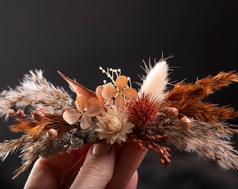 May include: A dried flower arrangement with a mix of brown, beige, and white dried flowers and grasses. The arrangement is held in a hand.