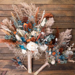 May include: A set of three dried flower bouquets in shades of brown, white, blue, and orange. The bouquets are made with pampas grass, dried flowers, and other natural elements. The bouquets are tied with twine and are ready to be displayed in a vase or used as wedding decor.