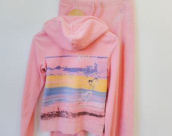 May include: Pink velour tracksuit with a graphic print of a sunset and hearts on the back of the jacket. The jacket has a hood and a zipper closure. The pants have a drawstring waistband. The text "juicy" is printed on the back of the pants.