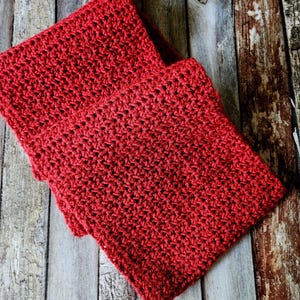 May include: Two red crocheted squares are stacked on a weathered wooden surface. The crochet stitch creates a textured pattern. The squares are a vibrant shade of red, and the wooden background has a rustic, aged appearance.
