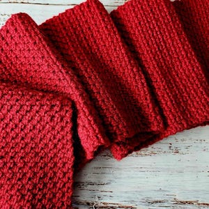 May include: A red knitted scarf folded on a white wooden surface.