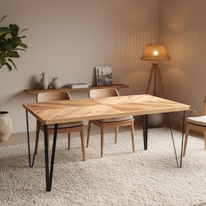 May include: A light wood dining table with black hairpin legs, surrounded by matching chairs. A large rug and a potted plant are in the foreground. A wooden lamp and a shelf with decor are in the background.