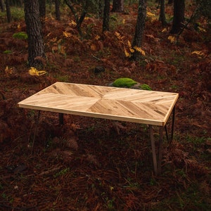 May include: A rectangular wooden table with a chevron pattern on the tabletop. The table has a light brown finish and dark metal hairpin legs. The table is approximately 60 inches long and 30 inches wide.