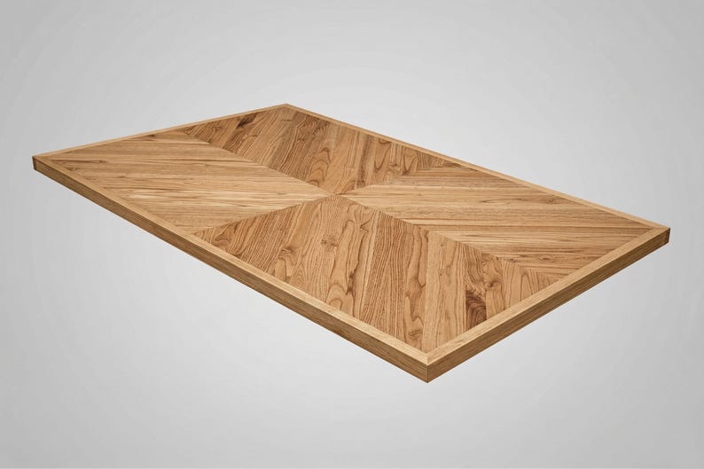 May include: Rectangular wooden tabletop with a light brown finish. The tabletop features a geometric pattern of angled wood grain, framed by a darker border. The design is symmetrical and modern, suitable for a dining or coffee table.