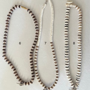 May include: Three necklaces made of brown and white beads. The necklaces are all different lengths and have different patterns. The necklaces are labeled 6, 7, and 8.