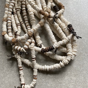 May include: A multi-strand necklace made of white and brown beads. The beads are round and have a smooth texture. The necklace is decorated with small metal charms.