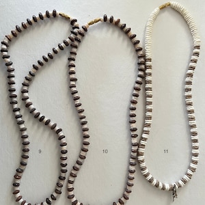 May include: Three necklaces made of brown and white beads. The necklaces are hanging on a white background. The necklaces are numbered 9, 10, and 11.