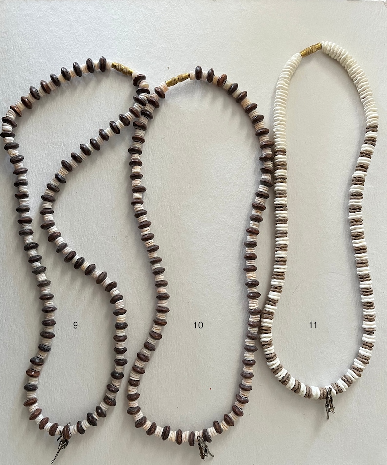 May include: Three necklaces made of brown and white beads. The necklaces are hanging on a white background. The necklaces are numbered 9, 10, and 11.