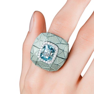 Könnte beinhalten: Ein silberner Ring mit einem hellblauen Edelstein und kleinen Diamanten, die in einem geometrischen Design gefasst sind.
