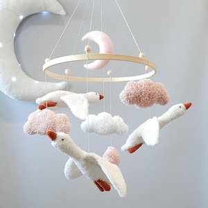 May include: A white wooden baby mobile with three white geese, two pink fluffy clouds, one white fluffy cloud, and a pink crescent moon.