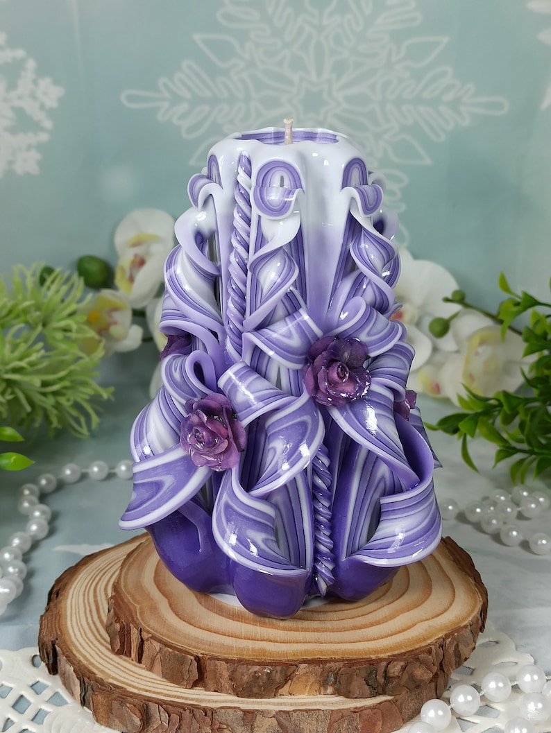 Puede incluir: Una vela tallada a mano de color morado y blanco con un dise&ntilde;o de espiral y tres rosas moradas. La vela est&aacute; sentada sobre una base de madera.