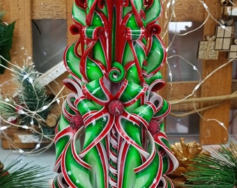 May include: A red and green Christmas candle with a decorative, intricate design. The candle is on a wooden base.