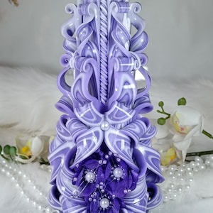 May include: A hand-carved candle with a purple and white swirl design. The candle is decorated with purple flowers and white pearls.