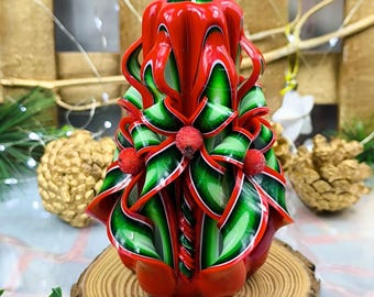 May include: A red and green hand-carved candle with a holly design. The candle is decorated with red berries and green leaves.