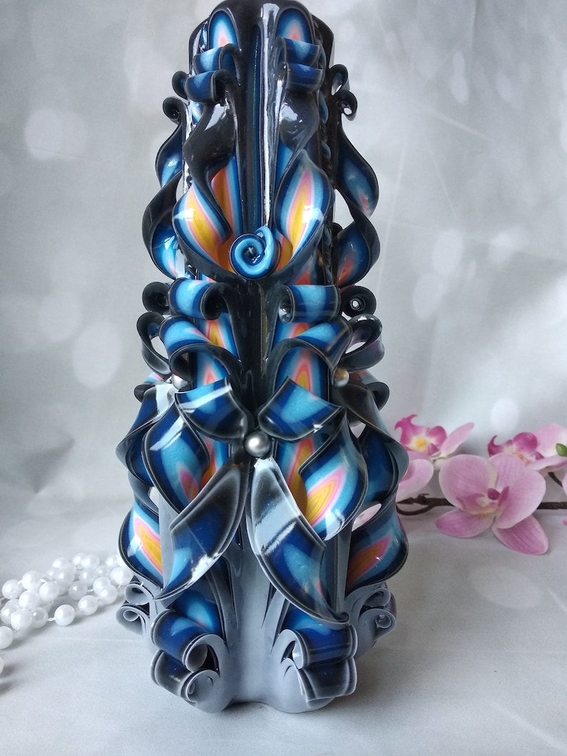 Puede incluir: Una vela alta y tallada de forma intrincada con un dise&ntilde;o de espiral negro, azul, blanco y amarillo. La vela est&aacute; decorada con peque&ntilde;as cuentas plateadas.