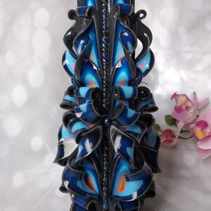 Puede incluir: Una vela tallada negra y azul con detalles intrincados. La vela est&aacute; decorada con remolinos y cintas, y tiene un dise&ntilde;o de cuerda negra y blanca en el centro.