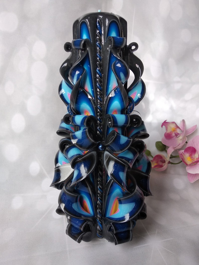 Puede incluir: Una vela tallada negra y azul con detalles intrincados. La vela est&aacute; decorada con remolinos y cintas, y tiene un dise&ntilde;o de cuerda negra y blanca en el centro.