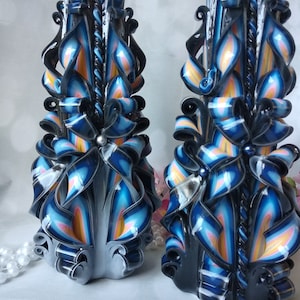 Puede incluir: Dos velas talladas con un esquema de color negro, blanco, azul y rosa. Las velas est&aacute;n decoradas con cintas y espirales.