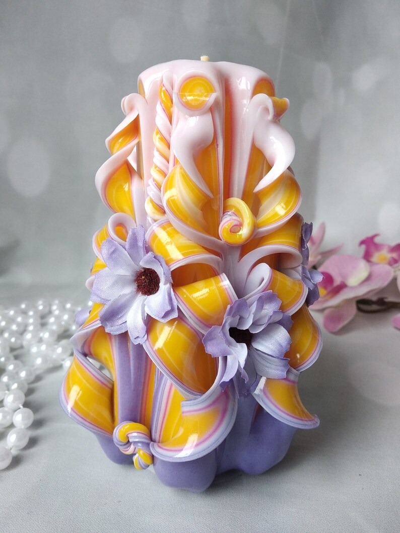 May include: A hand-carved candle with a purple, yellow, and pink striped design. The candle is decorated with three purple flowers.