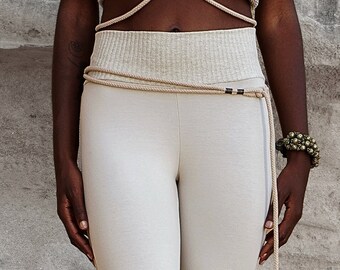 May include: A beige crop top and high-waisted leggings are paired with a rope belt. The top features a halter-style design, and the leggings are a solid color. A bracelet with round beads is on the right wrist. The outfit is neutral-toned.