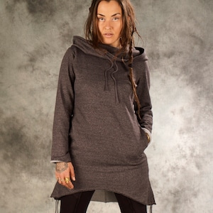 May include: A gray hooded sweatshirt with a long, asymmetrical hemline. The sweatshirt has a drawstring hood and a relaxed fit. The model is wearing black leggings and black boots.