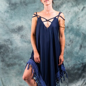 Op de afbeelding: Een vrouw draagt een donkerblauwe maxi-jurk met een gehaakte rand en franjes. De jurk heeft een gekruiste banddetail en een V-hals. Ze draagt zwarte enkellaarsjes.