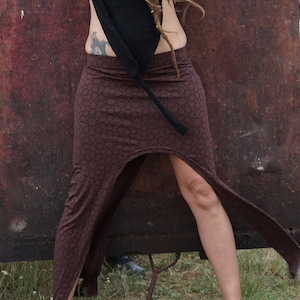 Puede incluir: Una falda marrón con un patrón geométrico y una abertura alta. La falda está hecha de una tela suave y fluida y tiene un ajuste holgado.