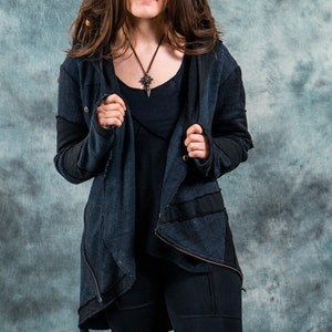May include: A woman wearing a dark blue hooded jacket with a black zipper and a black shirt underneath. She is wearing black pants with a silver necklace with a pendant.