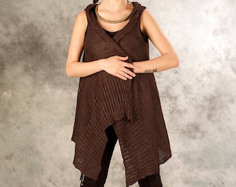 May include: A brown knitted sleeveless vest with a hood and a long, asymmetrical hem. The vest has a ribbed texture and is worn over a black top and pants.