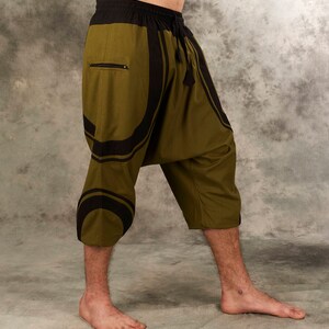 Puede incluir: Pantal&oacute;n de color verde oliva y negro con estampado, con cintura de cord&oacute;n y bolsillo con cremallera. El pantal&oacute;n es corto y de corte holgado.