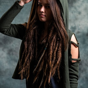 May include: A woman with long brown dreadlocks wears a dark green hooded sweater with a distressed look. The sweater has cut-out details on the shoulders and sleeves.