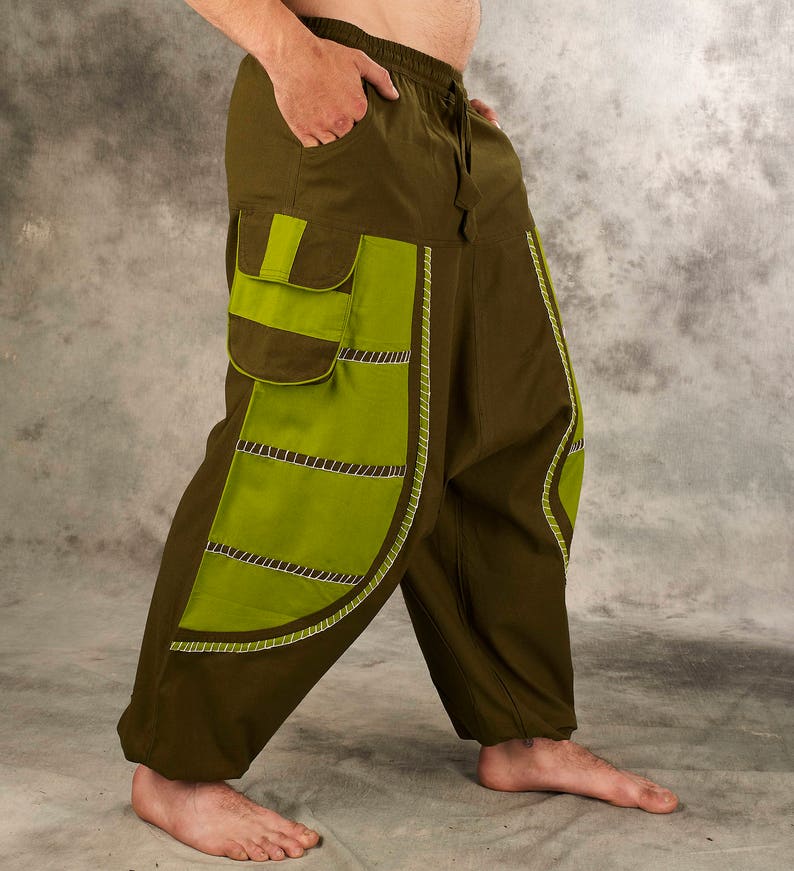 May include: Olive green pants with a large green and brown patch on the left leg. The patch has a white stitched design.