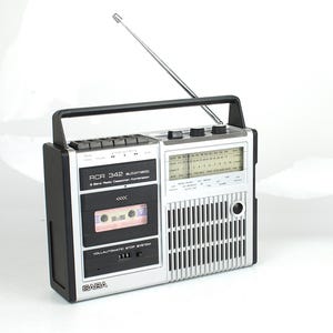 Op de afbeelding: Een zilverkleurige en zwarte SABA RCR 342 automatic 8 band radio-cassettespeler. Het apparaat is voorzien van een handvat aan de bovenzijde, een uitschuifbare metalen antenne, een cassettedeck, een luidsprekerrooster en een radiofrequentiepaneel.