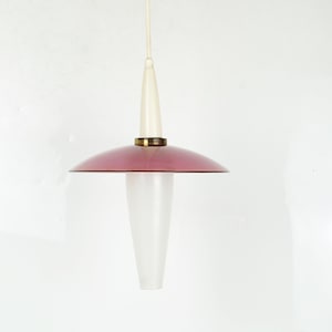 Può includere: Una lampada a sospensione vintage con una parte superiore bianca e un paralume color malva. La lampada ha una base in vetro smerigliato e un anello color ottone. La lampada è appesa a un cavo bianco.