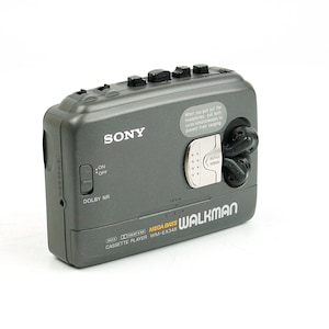 May include: A dark gray Sony Walkman cassette player model WM-EX348 featuring Mega Bass, Dolby NR, and an on/off switch. The device includes a silver latch, black control buttons on the top edge, and a small circular area for storing earbuds.