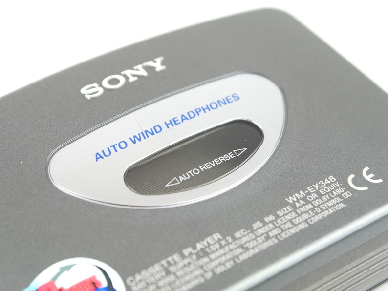 May include: A grey Sony cassette player featuring a silver oval window with the blue text AUTO WIND HEADPHONES and the black text AUTO REVERSE. The device includes the model number WM-EX348, a CE mark, and technical battery information printed in white.