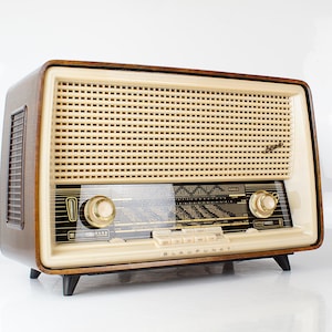 Puede incluir: Radio Blaupunkt vintage con una rejilla de altavoz color crema y una carcasa de chapa de madera oscura. La radio tiene perillas doradas y un dial transparente con indicadores de estación. La palabra "Blaupunkt" está impresa en la parte delantera.