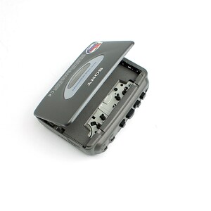 May include: A dark gray Sony Walkman cassette player with the cassette compartment door partially open. The device features a silver oval accent on the lid, black control buttons on the side, and internal mechanical components visible inside.