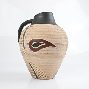 May include: A beige ceramic vase with a black rim and a brown and black abstract design. The vase has a textured surface and a narrow neck.