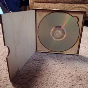 May include: A wooden CD case with a hinged lid, open to reveal a blank CD inside.
