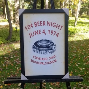 May include: A framed poster advertising a 10&cent; Beer Night at Cleveland, Ohio's Municipal Stadium on June 4, 1974. The poster features a black and white illustration of the stadium.